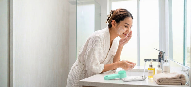 Frau bei der morgendlichen Gesichtsreinigung im modernen Badezimmer mit Lazurec Care Gesichtsreinigungsbürste und Augenmassagegerät auf dem Waschtisch.
